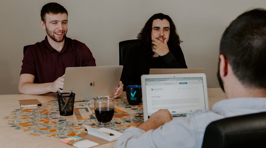 A group of people are sitting at a work table with their laptop computers