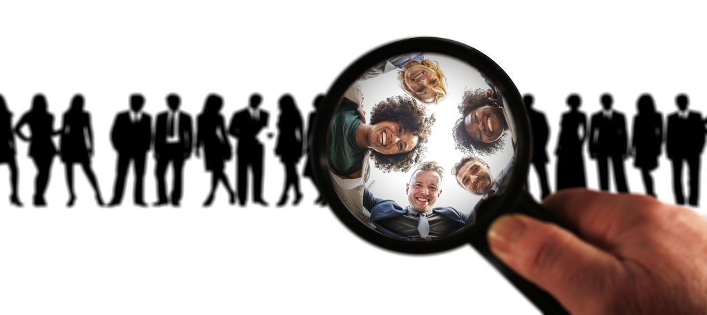 A group of men and woman are standing and under a magnifying glass