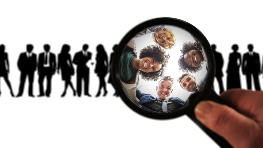 A group of men and woman are standing and under a magnifying glass