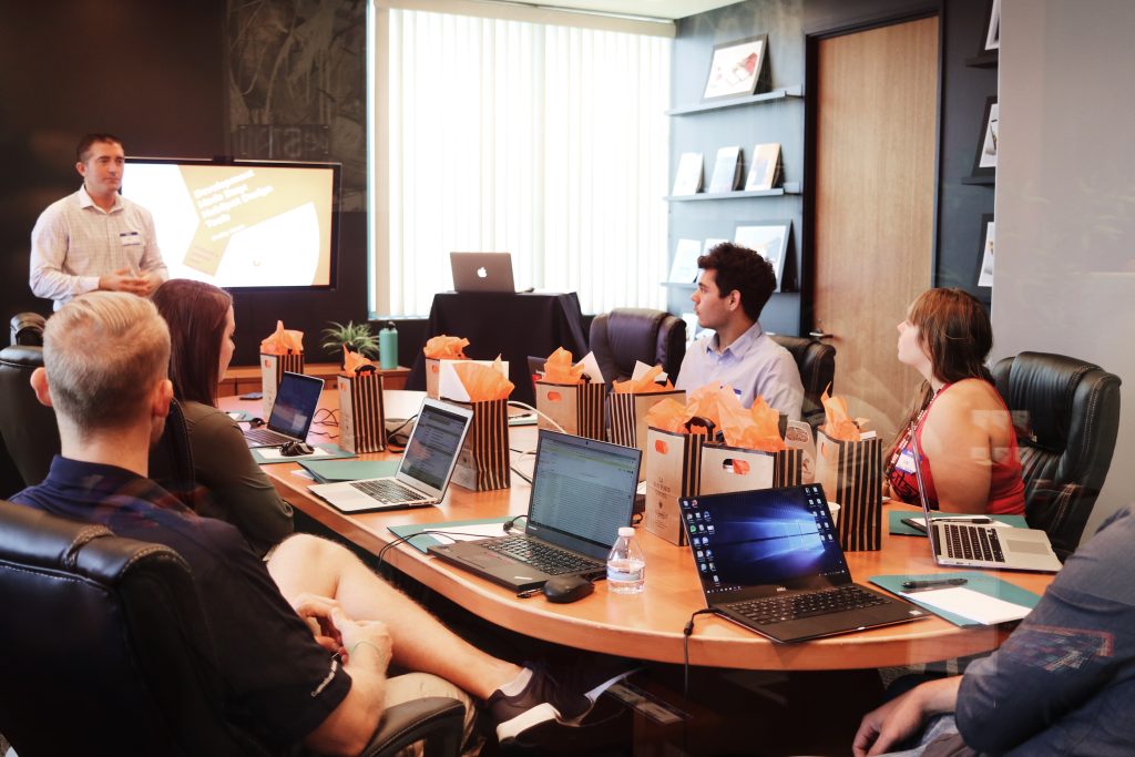 A large number of both men and woman are sitting around a conference table talking.