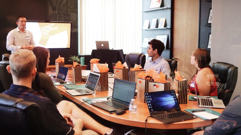 A large number of both men and woman are sitting around a conference table talking.