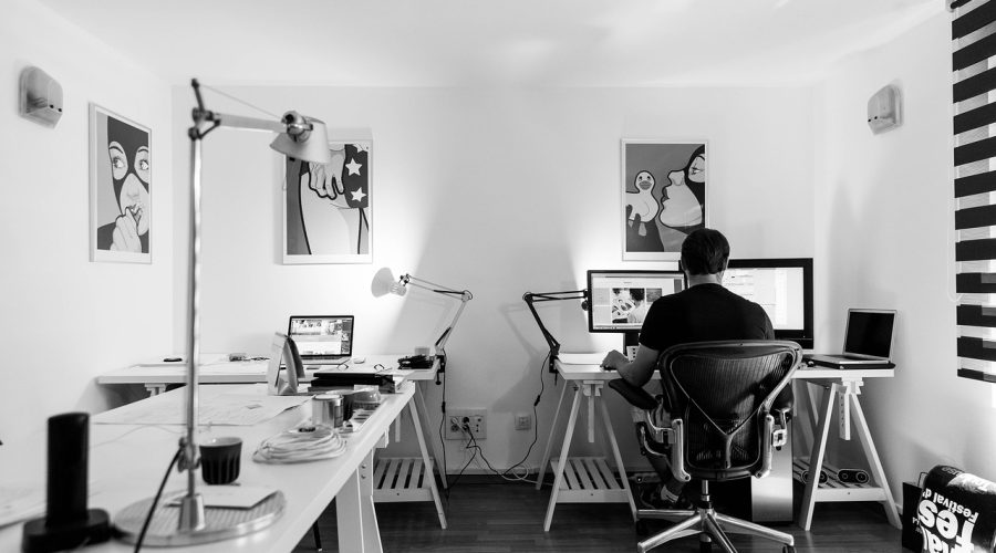 A man is sitting at a desk with computers, camera, cell phones