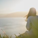 A woman is sitting on a bluff looking out over the ocean