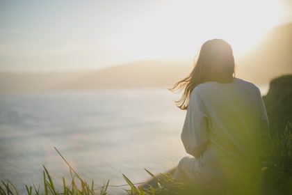 A woman is sitting on a bluff looking out over the ocean