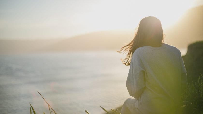 A woman is sitting on a bluff looking out over the ocean