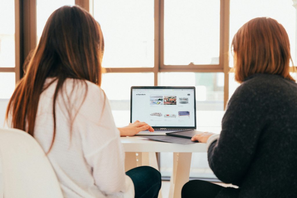 2 Woman are sitting at a desk looking at a computer screen