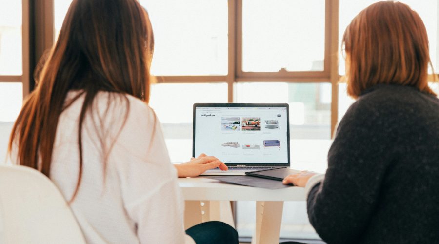 2 Woman are sitting at a desk looking at a computer screen