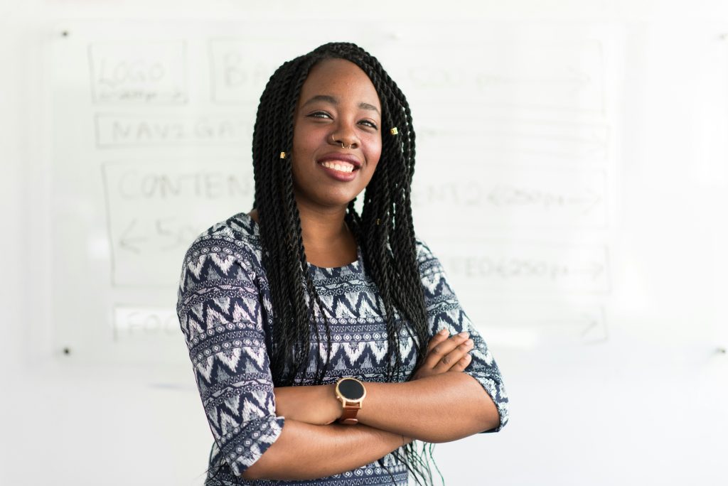 An African American woman is standing with her arms crossed and smiling