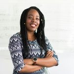 An African American woman is standing with her arms crossed and smiling