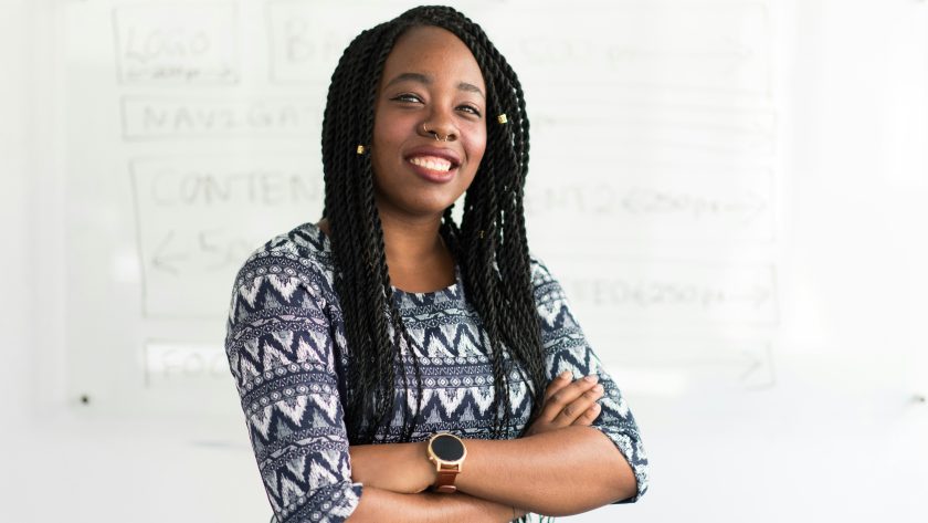 An African American woman is standing with her arms crossed and smiling