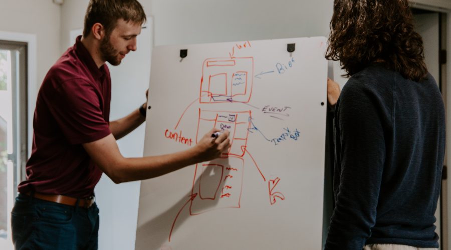 A man is standing in front of a white board and writing