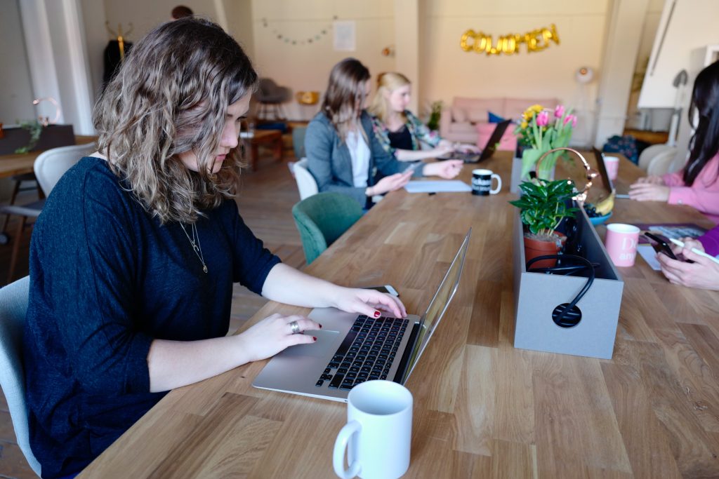 A group of people are sitting at a large table looking at their laptop computers