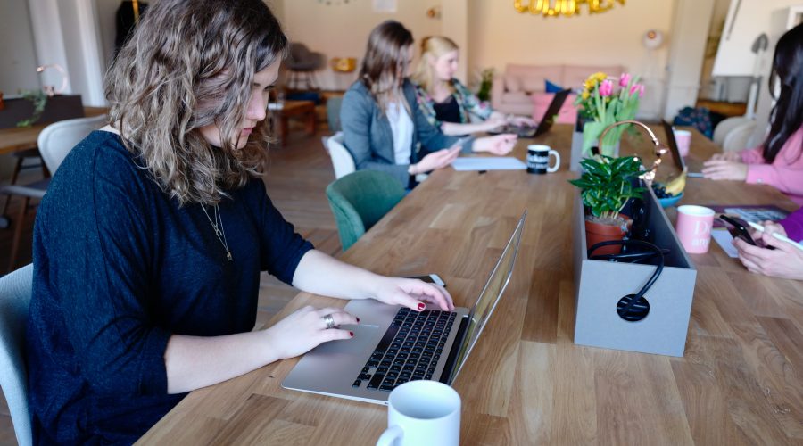 A group of people are sitting at a large table looking at their laptop computers