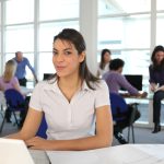 Smiling woman using a laptop in a busy office