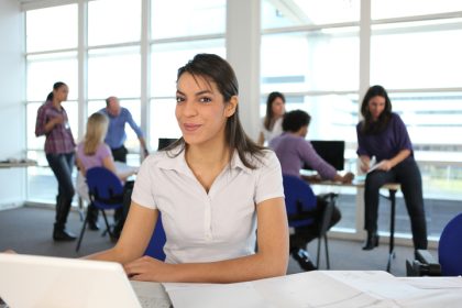 Smiling woman using a laptop in a busy office