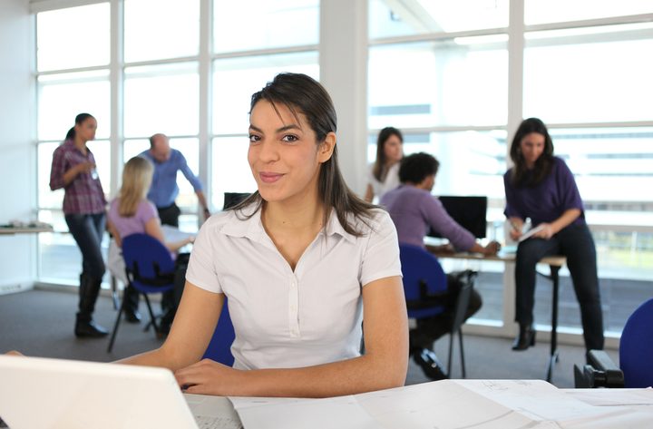 Smiling woman using a laptop in a busy office