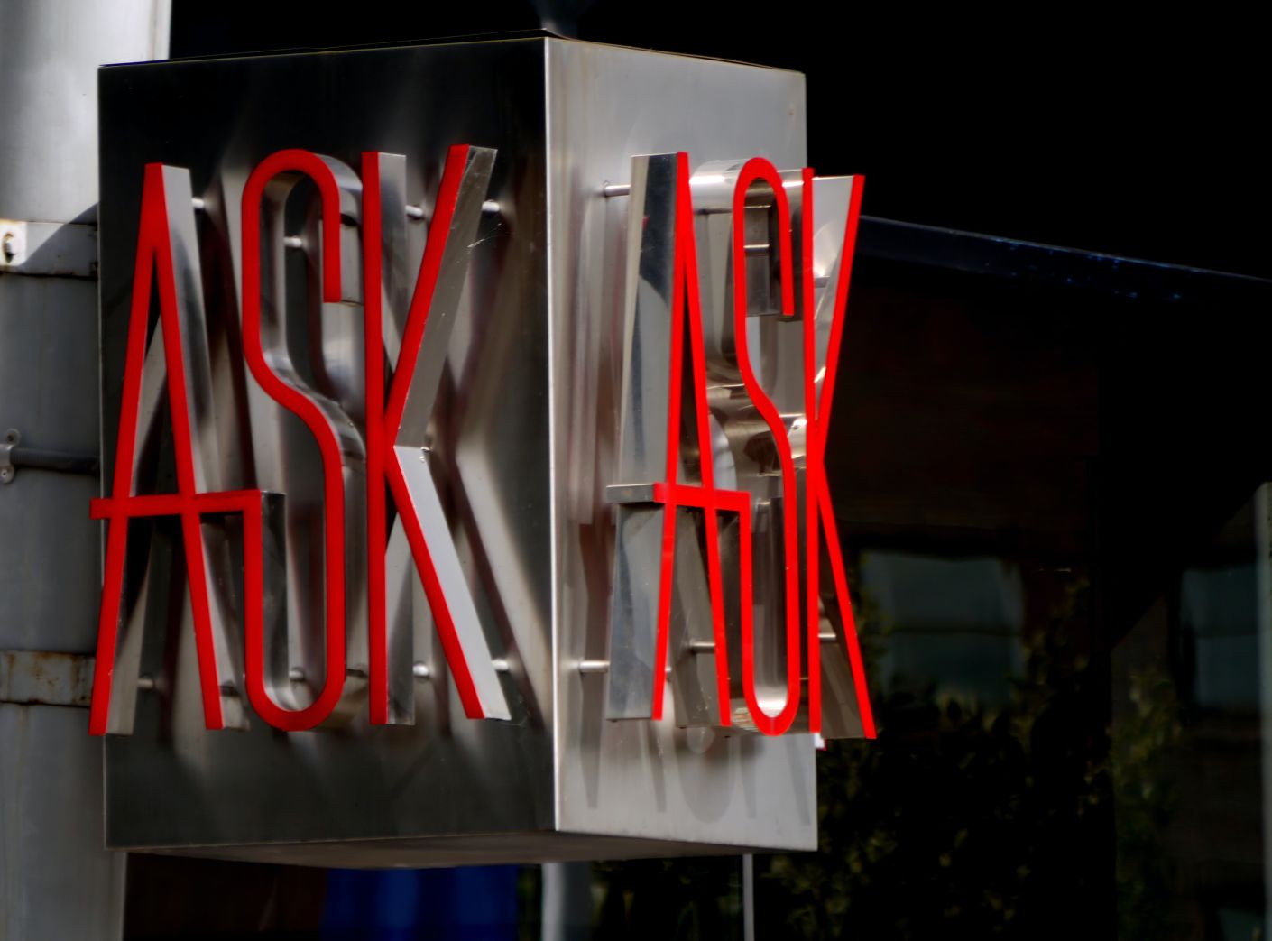 Silver sign on wall with the word ask in red letters